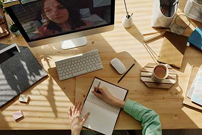 Person writing in notebook in front of computer