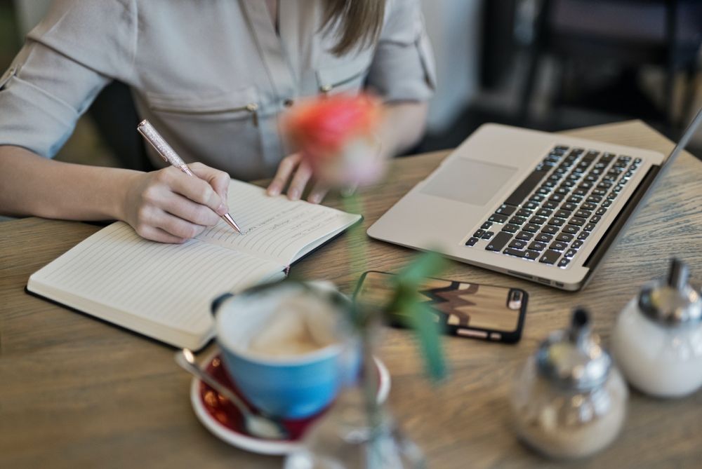 Person writing on paper beside laptop