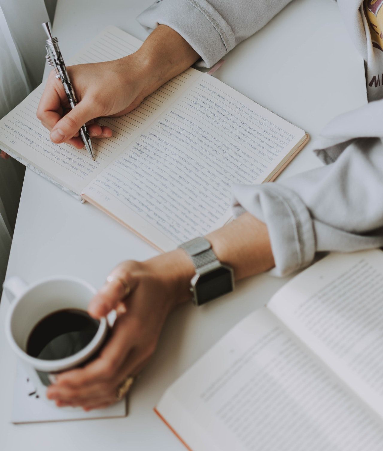 Person writing in notepad while holding cup of co